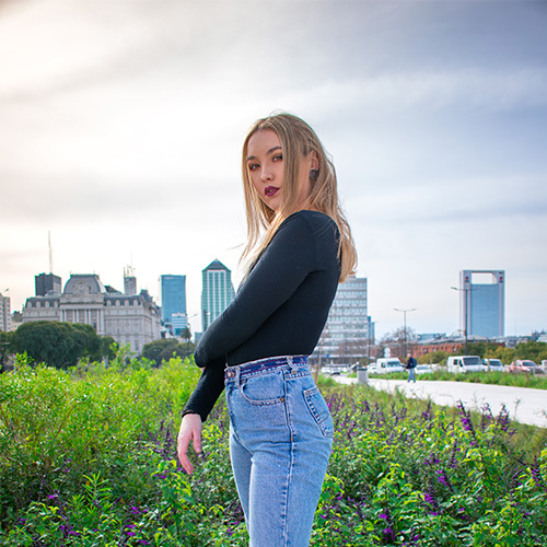 Foto de una chica rubia entre flores de lavanda, con la ciudad de fondo